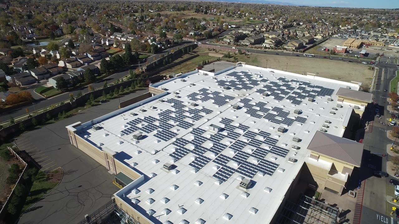Aerial frame in Hidden Lake, Colorado showing the large white roof with solar panels in the foreground, roads and homes behind it, and no visible people.