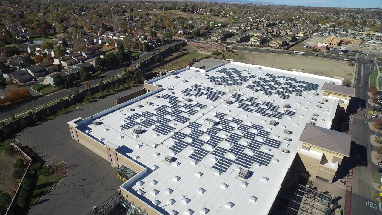 Drone-style aerial view over a solar-covered building roof and suburban neighborhood