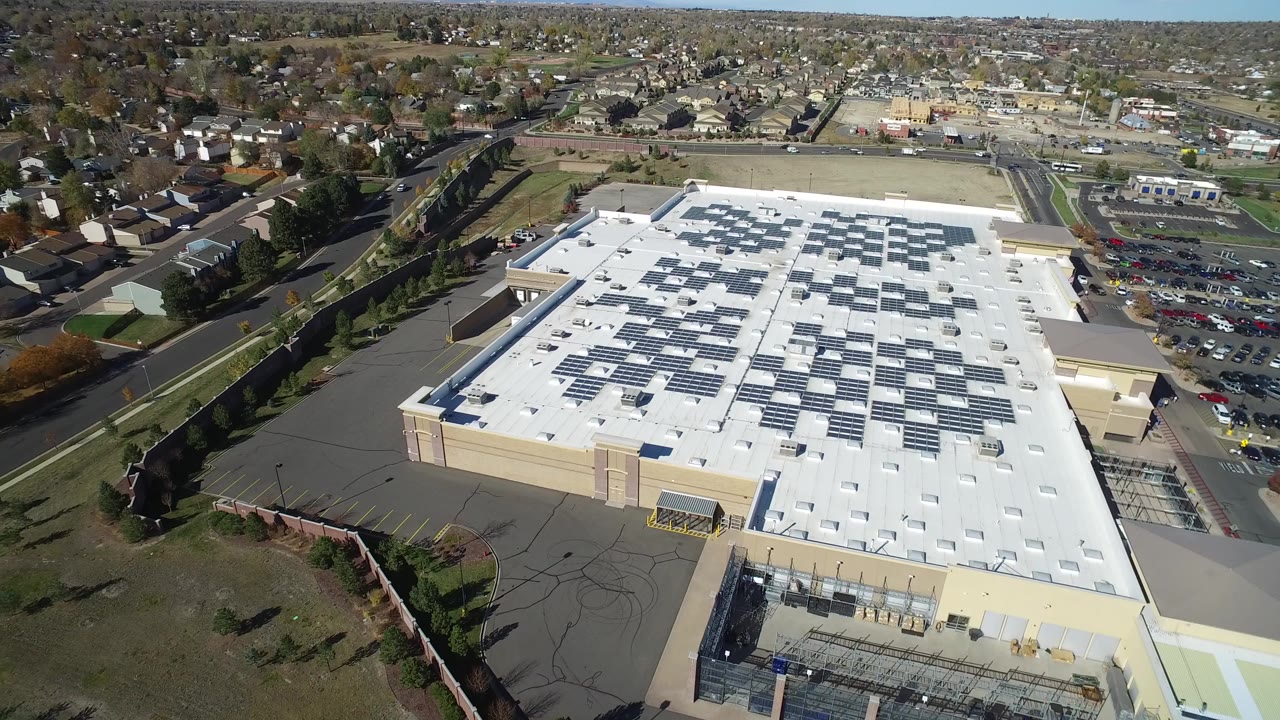 Aerial view of a large building with rooftop solar panels and surrounding roads