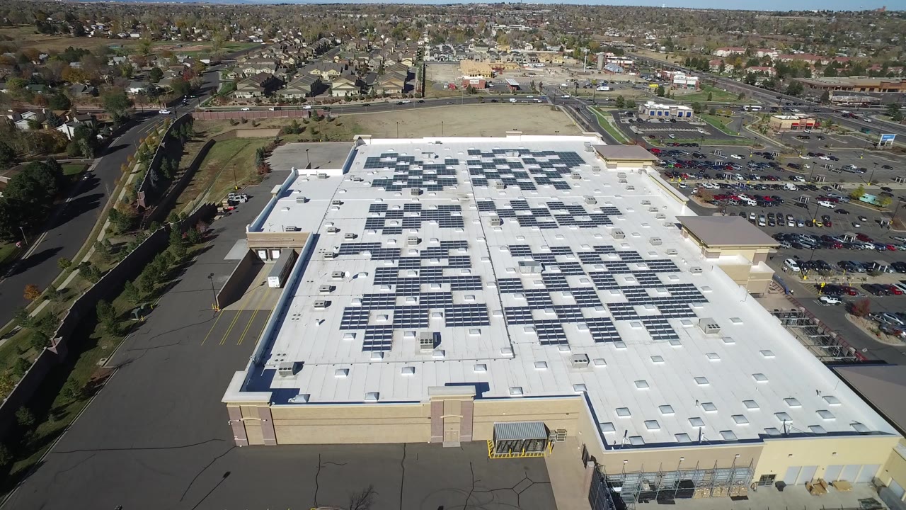 Aerial view of a large white commercial roof with solar panels and parking lot