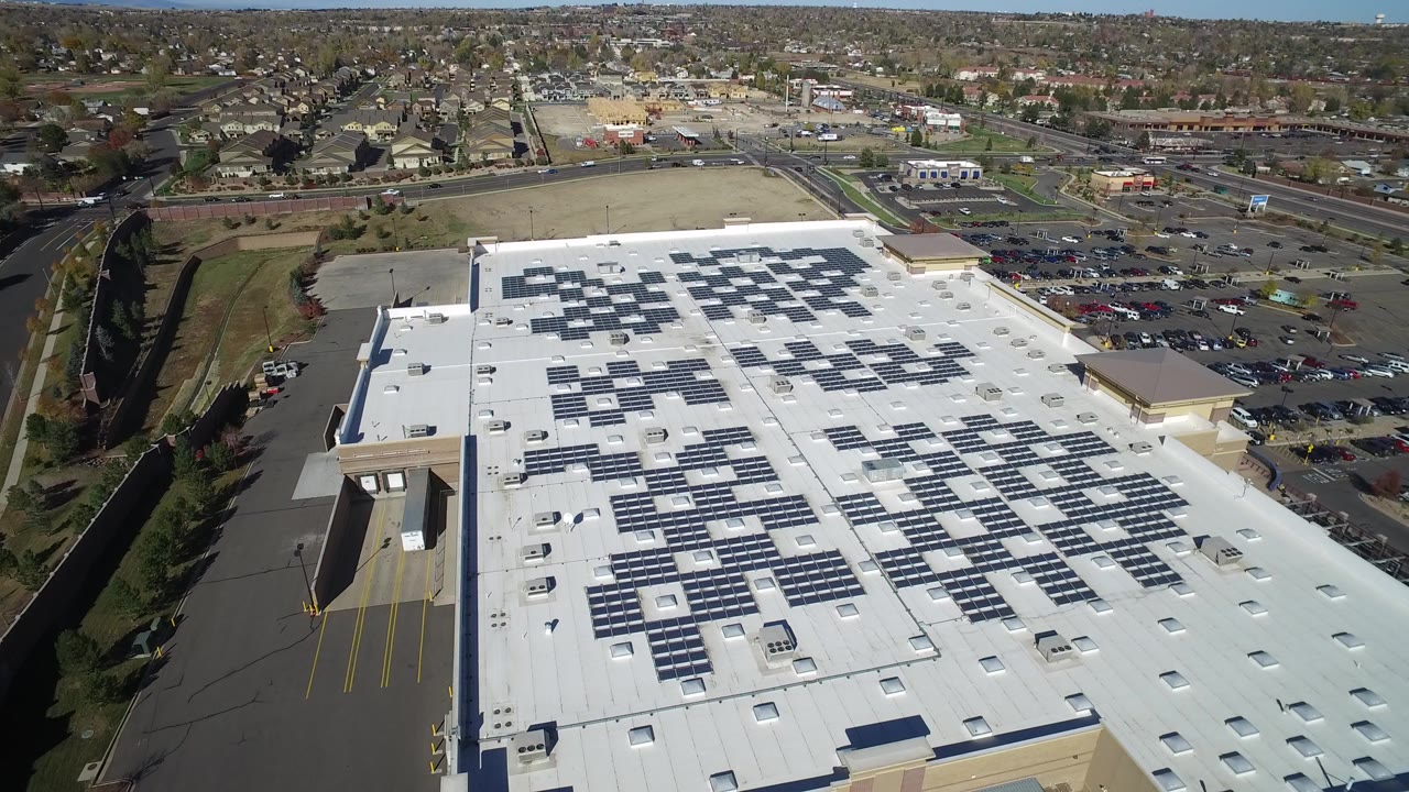 High aerial view of a large white-roofed commercial building with solar panels.