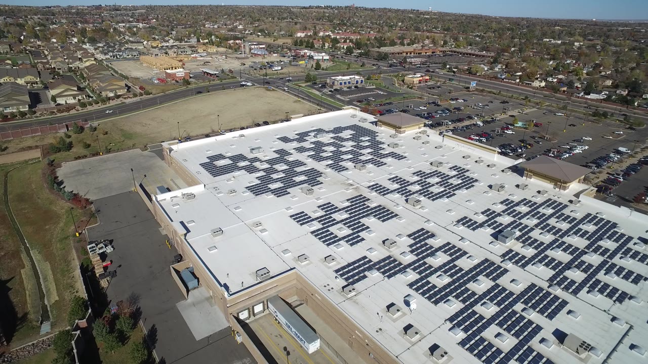 High drone composition in Hidden Lake, Colorado showing the solar-covered roof from a slightly farther right position, with cars in parking lots, arterial roads, and no visible people.
