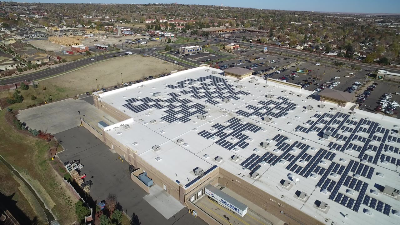 High aerial view of a commercial roof with solar panels and surrounding roads.