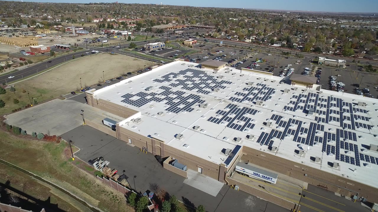 High aerial view of a warehouse roof with solar panels and surrounding roads.