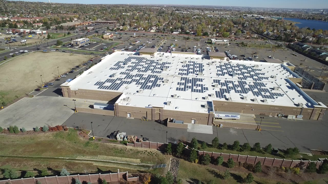Aerial view of a large white-roof building with solar panels and surrounding roads.