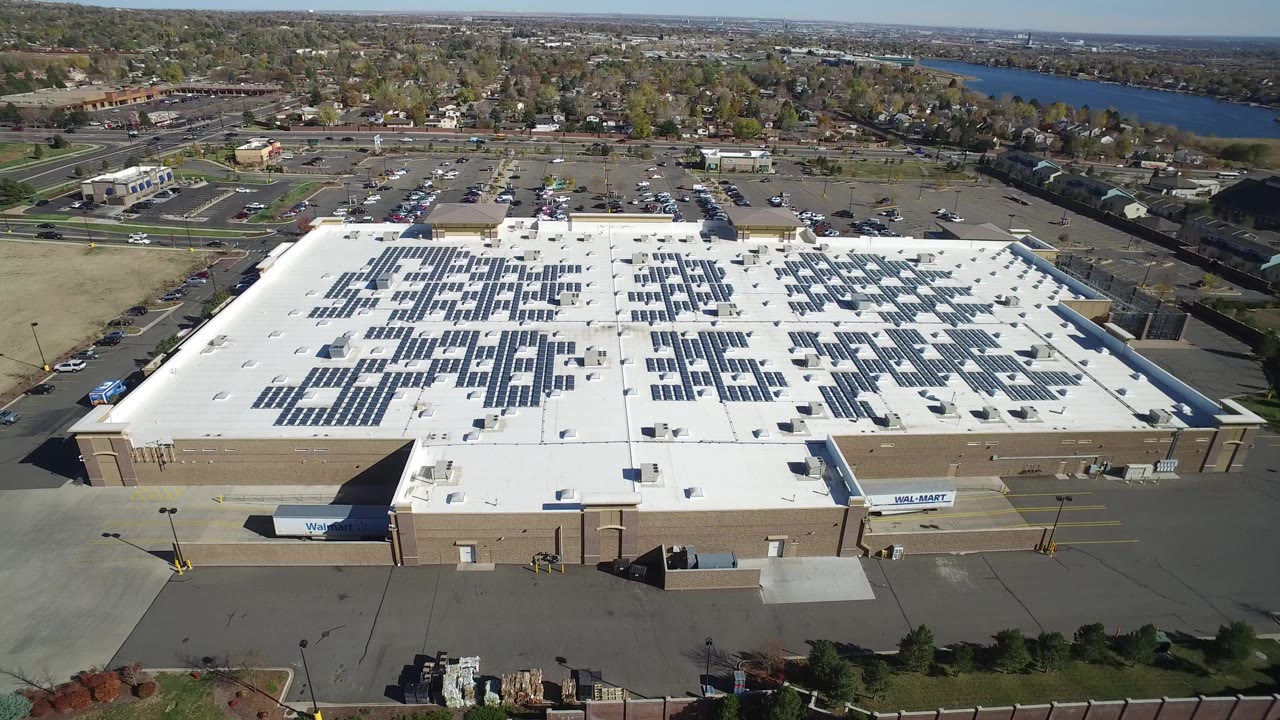 Aerial view of a large retail roof covered with solar panels near homes and a waterway.