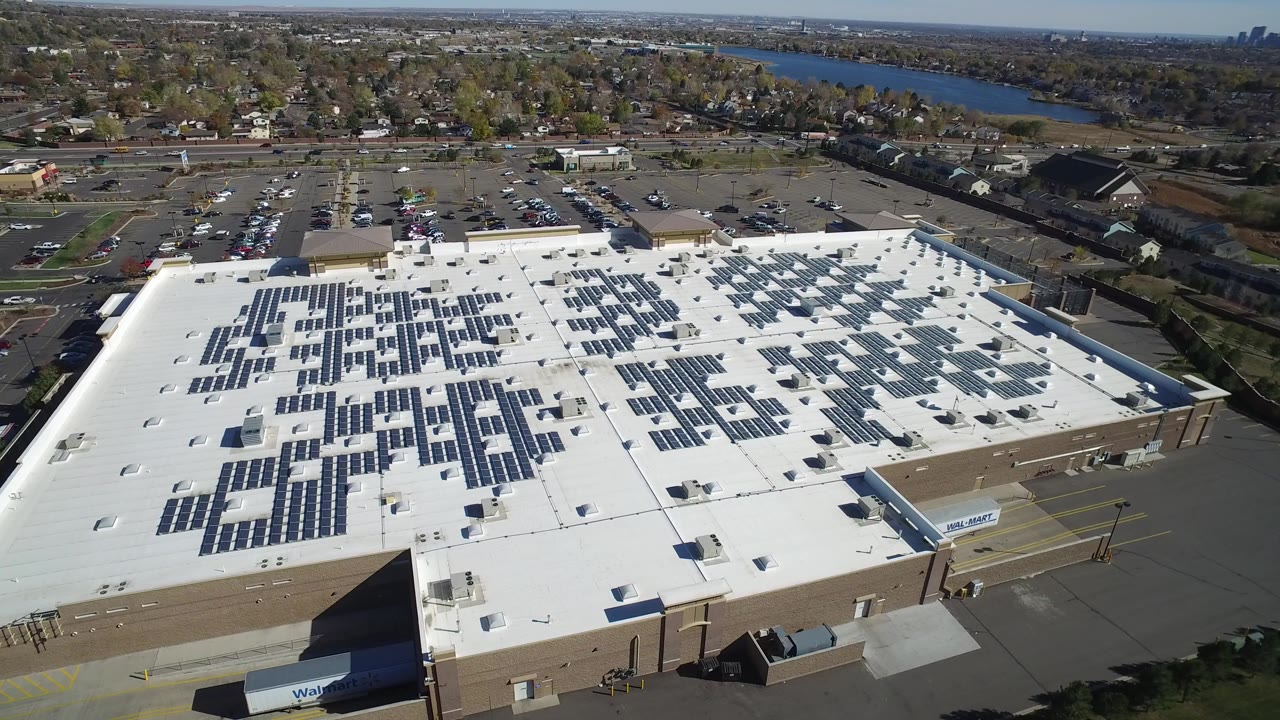 Aerial view of a white-roof commercial building with rows of solar panels.