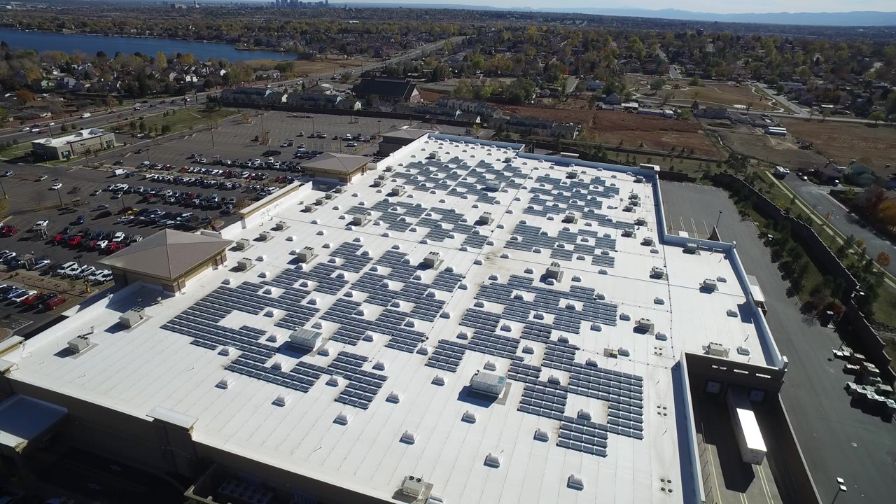 Aerial view of a large white-roofed building with solar panels and parking lots.