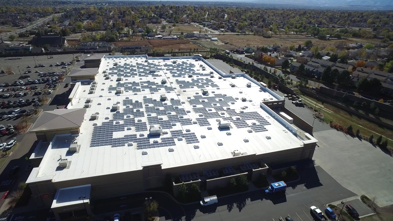 Aerial view of a large white-roofed building with solar panels and nearby parking lots.