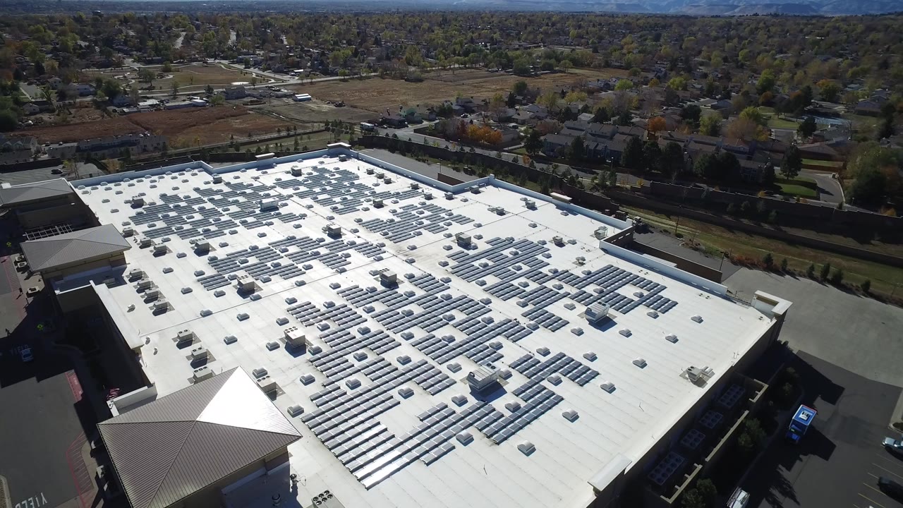 Aerial view of a white commercial roof with solar panels and suburban streets beyond.