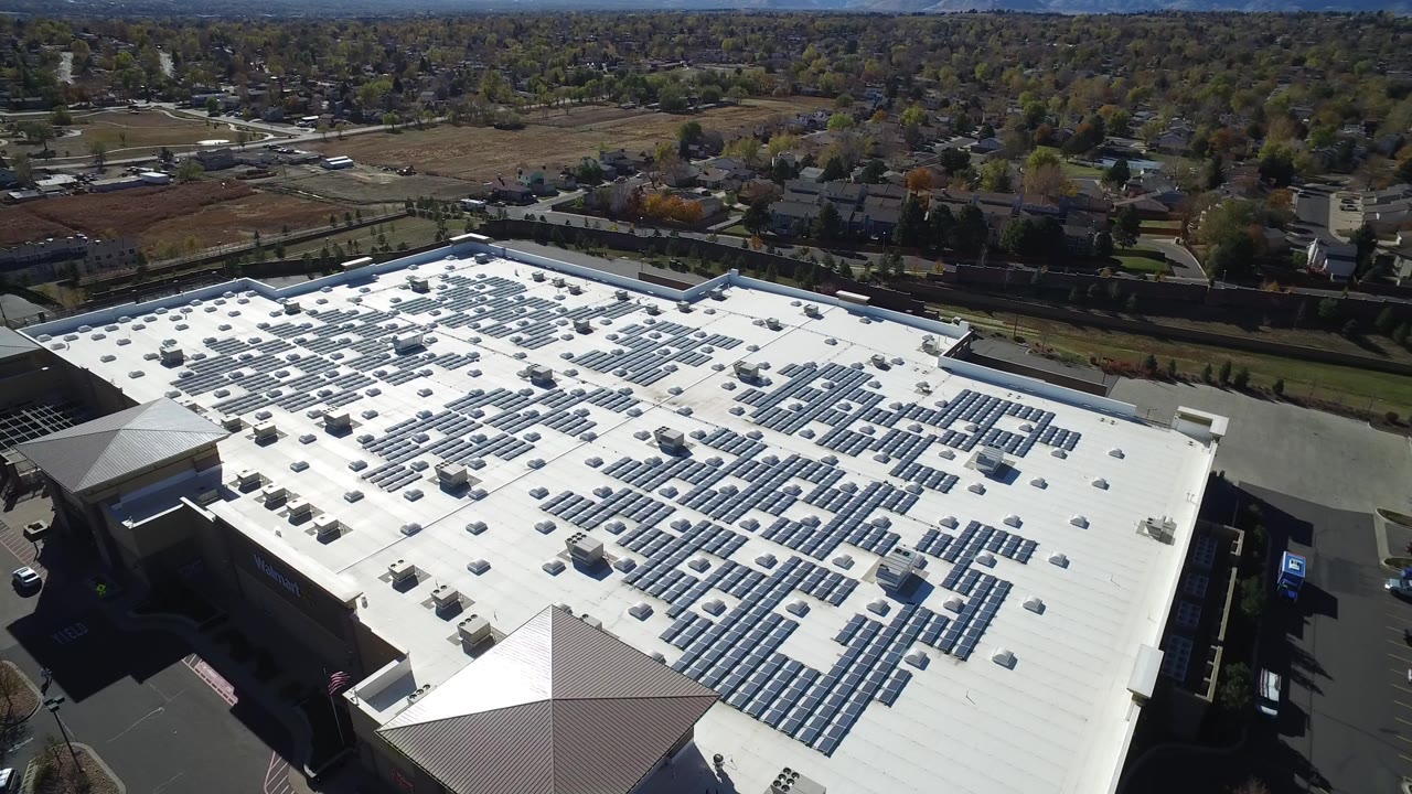 Aerial view of a large white-roofed commercial building with rooftop solar panels.