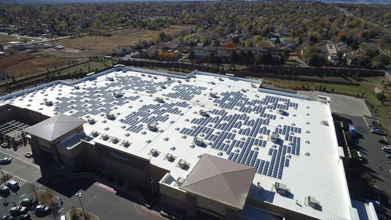 High aerial view of a large white-roofed retail building with solar panels and parking areas.