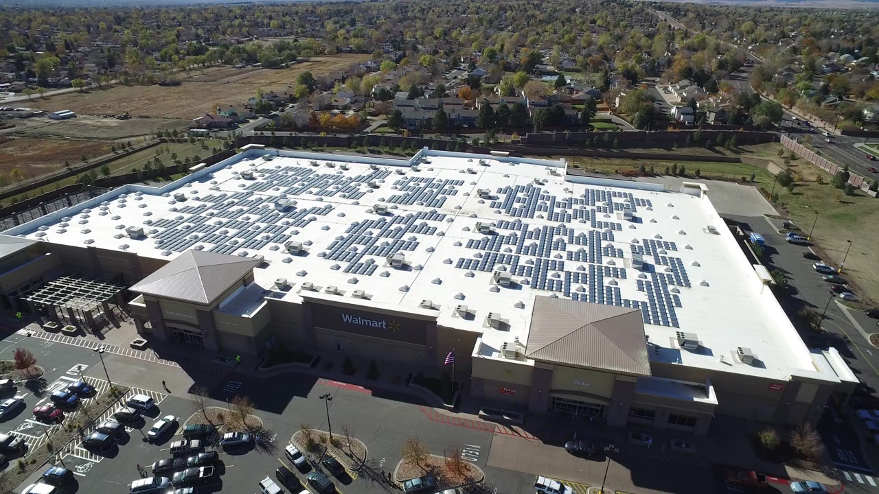 Elevated view in Hidden Lake, Colorado of a large retail building with a white roof, solar panels, parked cars, nearby roads, and no visible people.