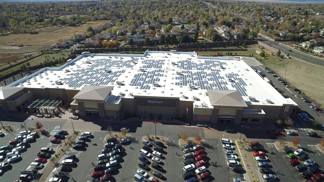 Aerial frame from Hidden Lake, Colorado showing a white-roofed big box store, parked cars in front, fields and homes beyond, and no visible people.