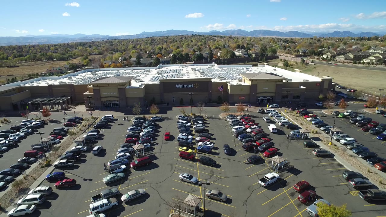 A second aerial view in Hidden Lake, Colorado holds on the Walmart building, packed parking rows, side roads, suburban rooftops, mountain skyline, and no visible people.