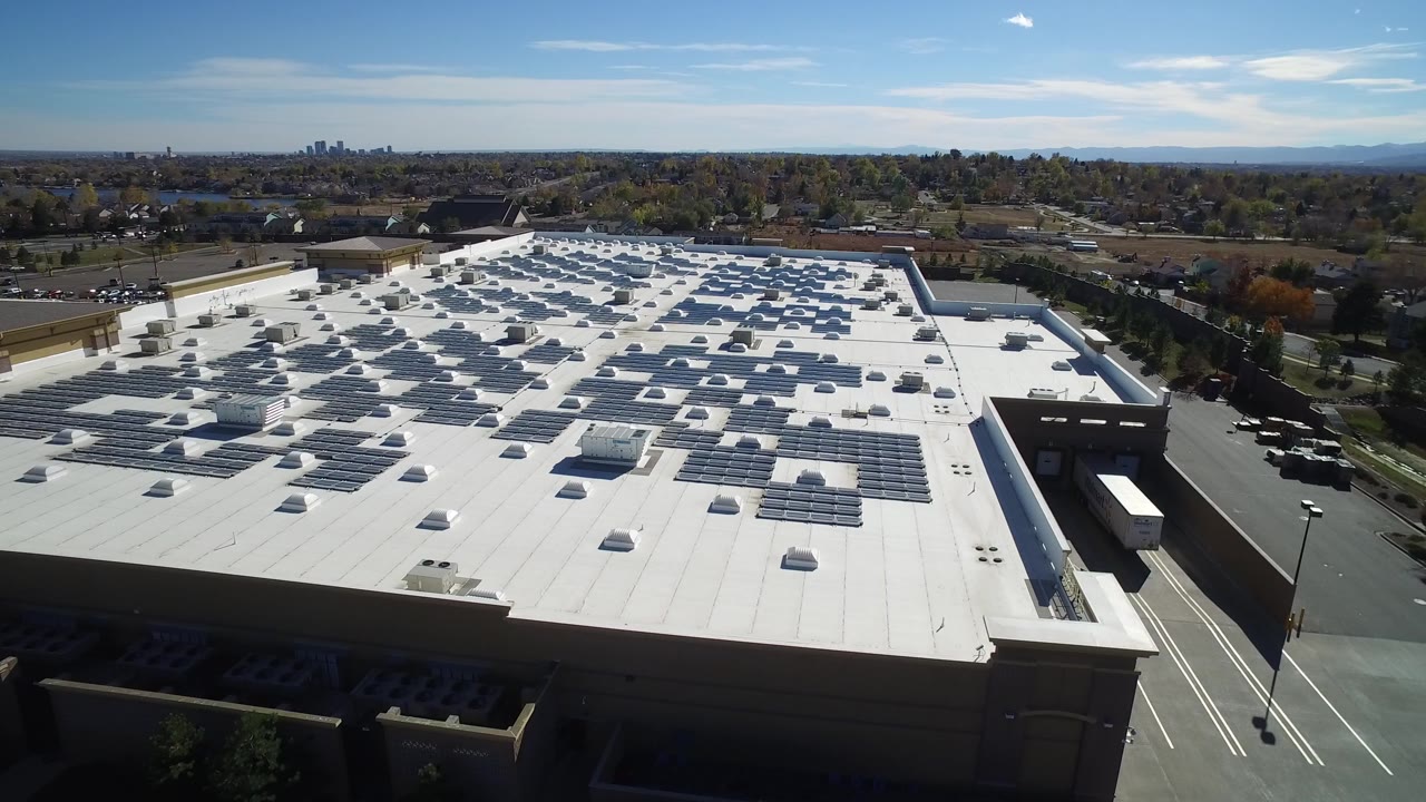 Aerial view of a large white commercial roof with solar panels.