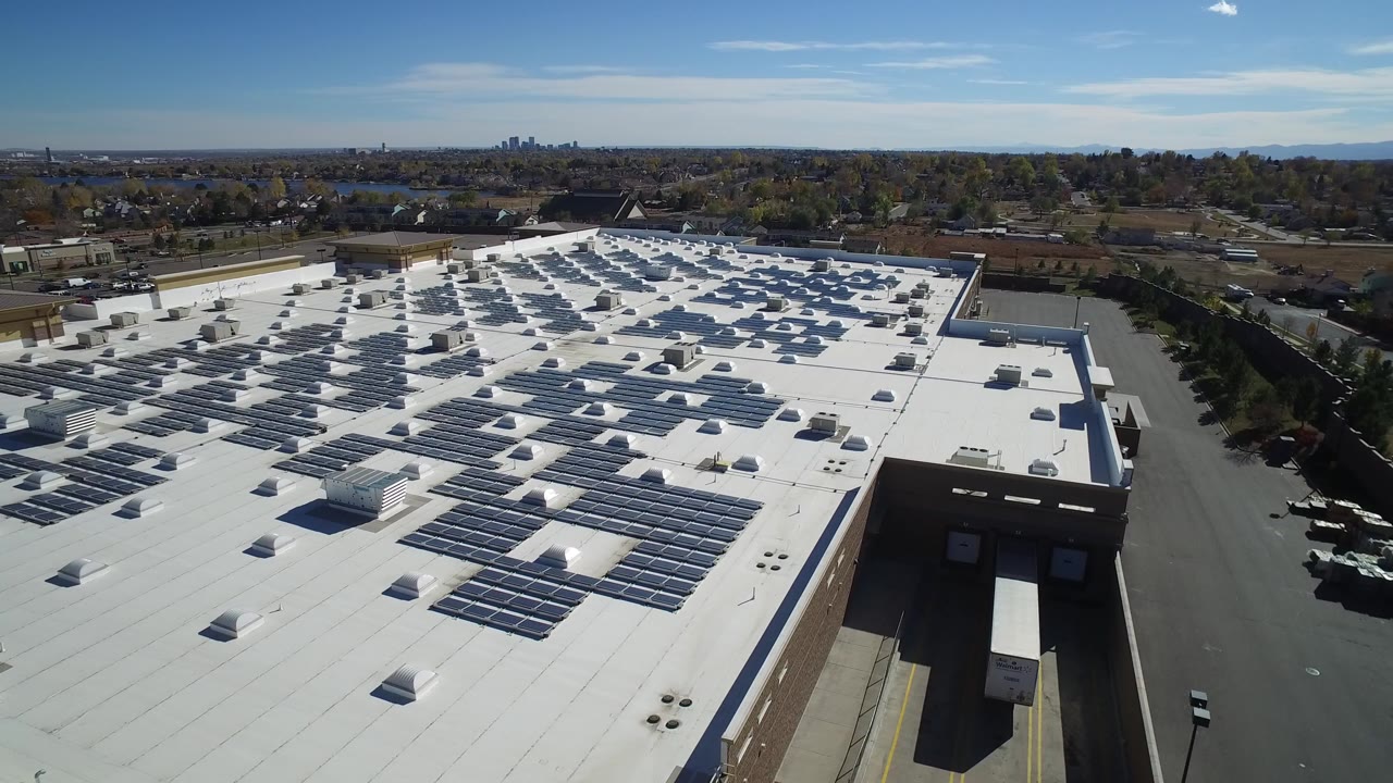 Aerial view of a white commercial roof covered with solar panels.