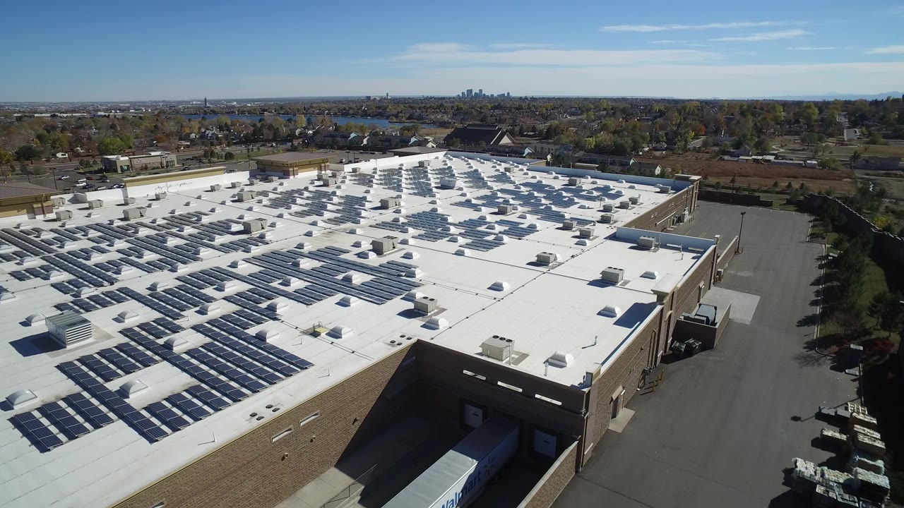 Aerial view of a white-roofed commercial building with solar panels and surrounding roads.