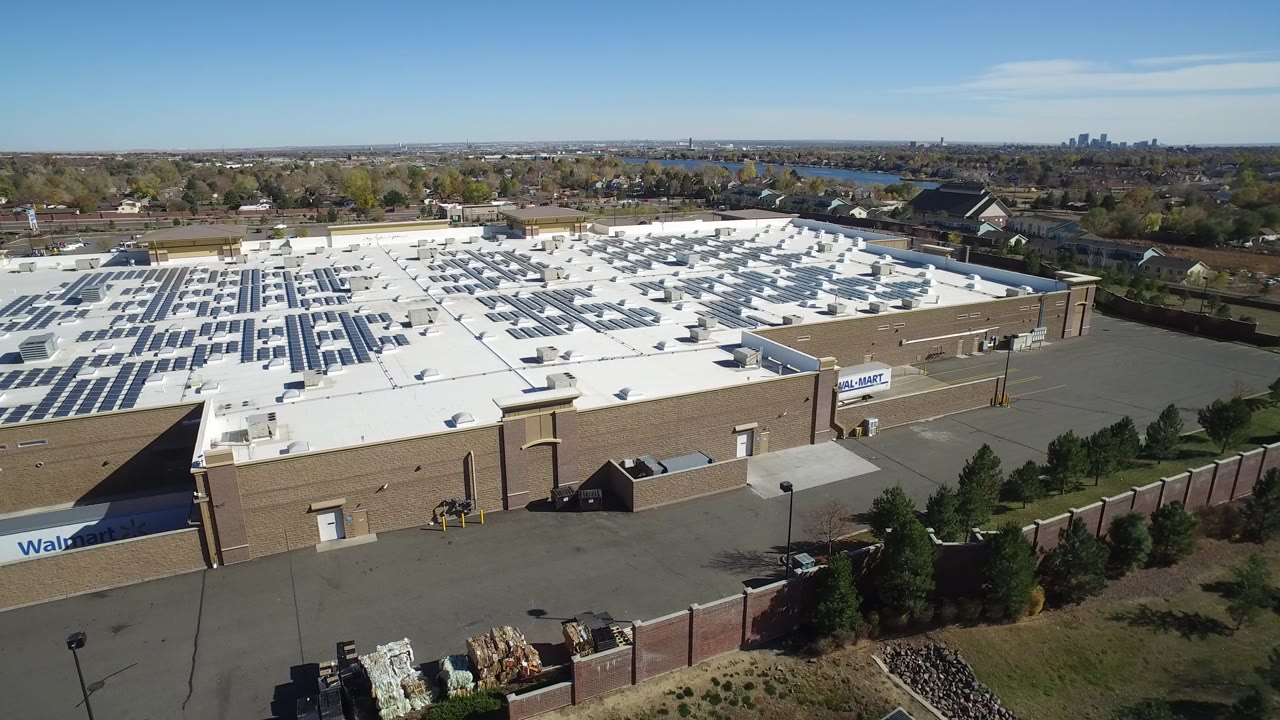 Aerial view of a large white-roofed retail building with solar panels and surrounding trees.