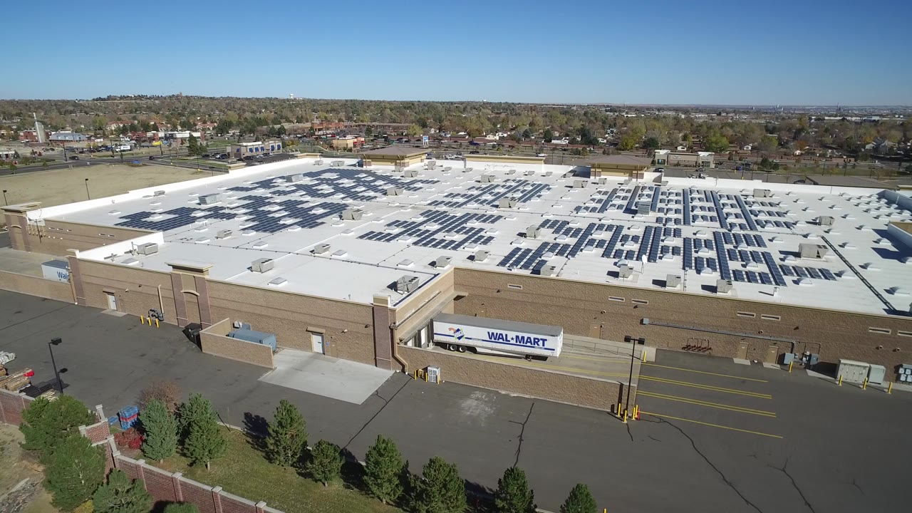 Elevated Hidden Lake, Colorado frame with the solar-panel grid centered on the white roof, the Walmart sign visible on the wall, a mostly empty paved area below, and no visible people.