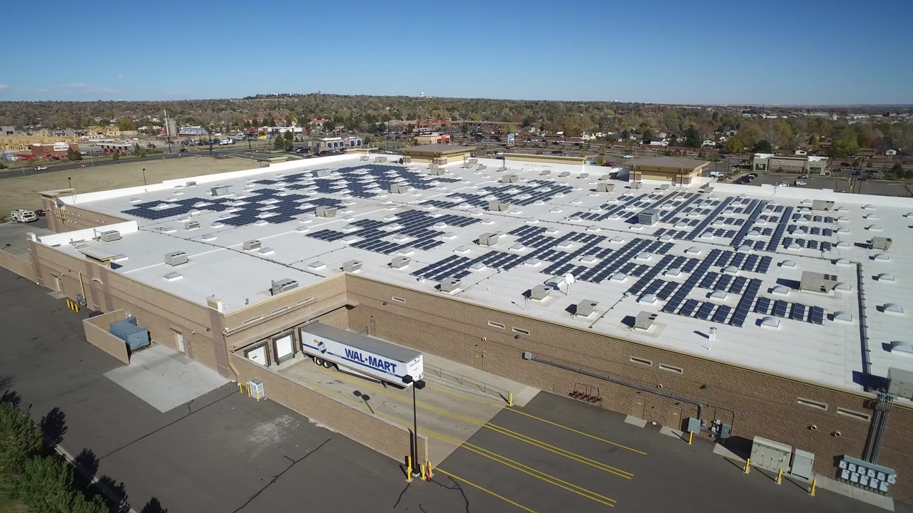 Aerial view of a tan industrial building with solar panels on a white flat roof.