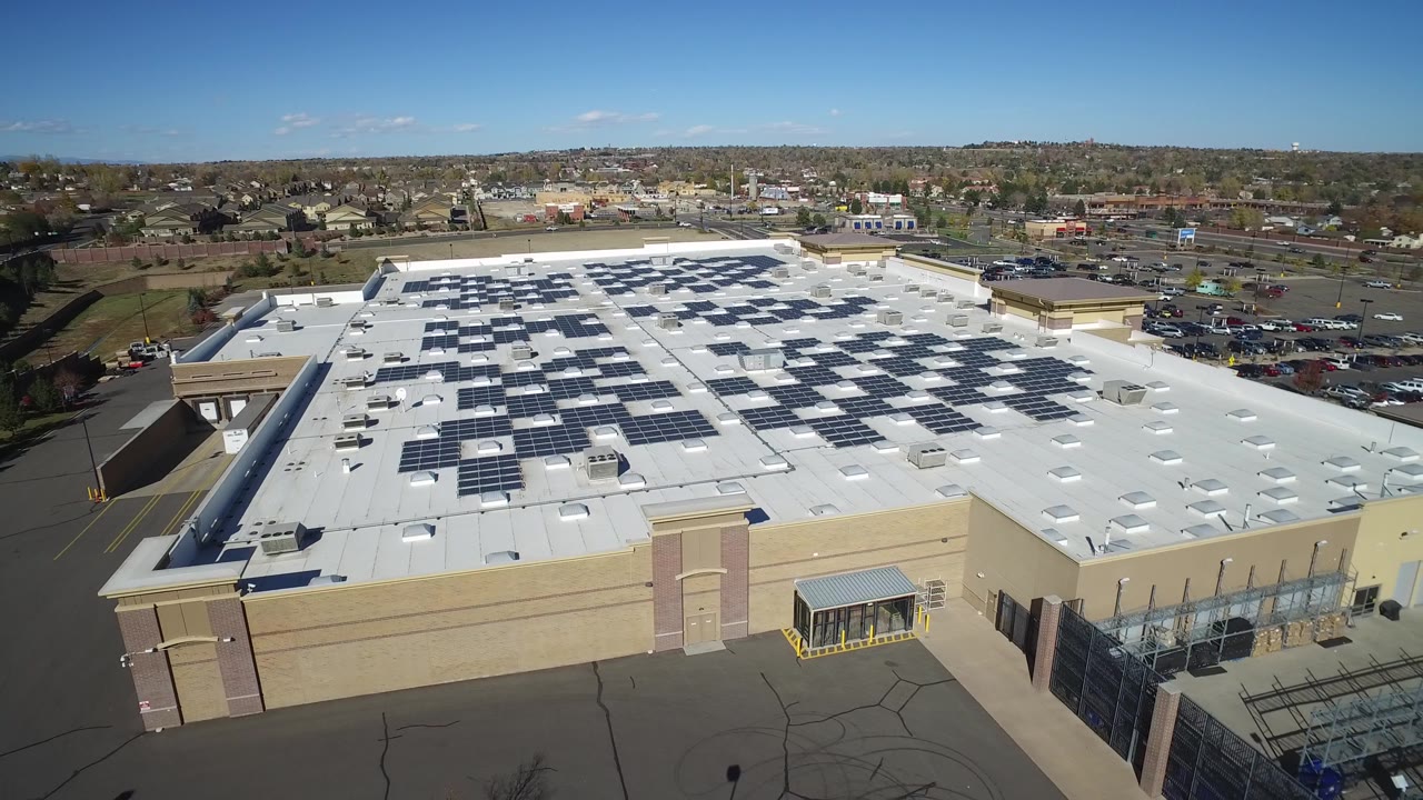 High angle view of a solar-covered roof beside asphalt lots and suburban streets.