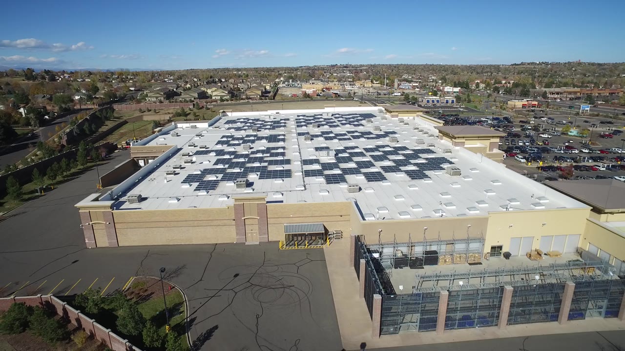 Overhead view of a commercial building roof with solar panels and parking lots beyond.