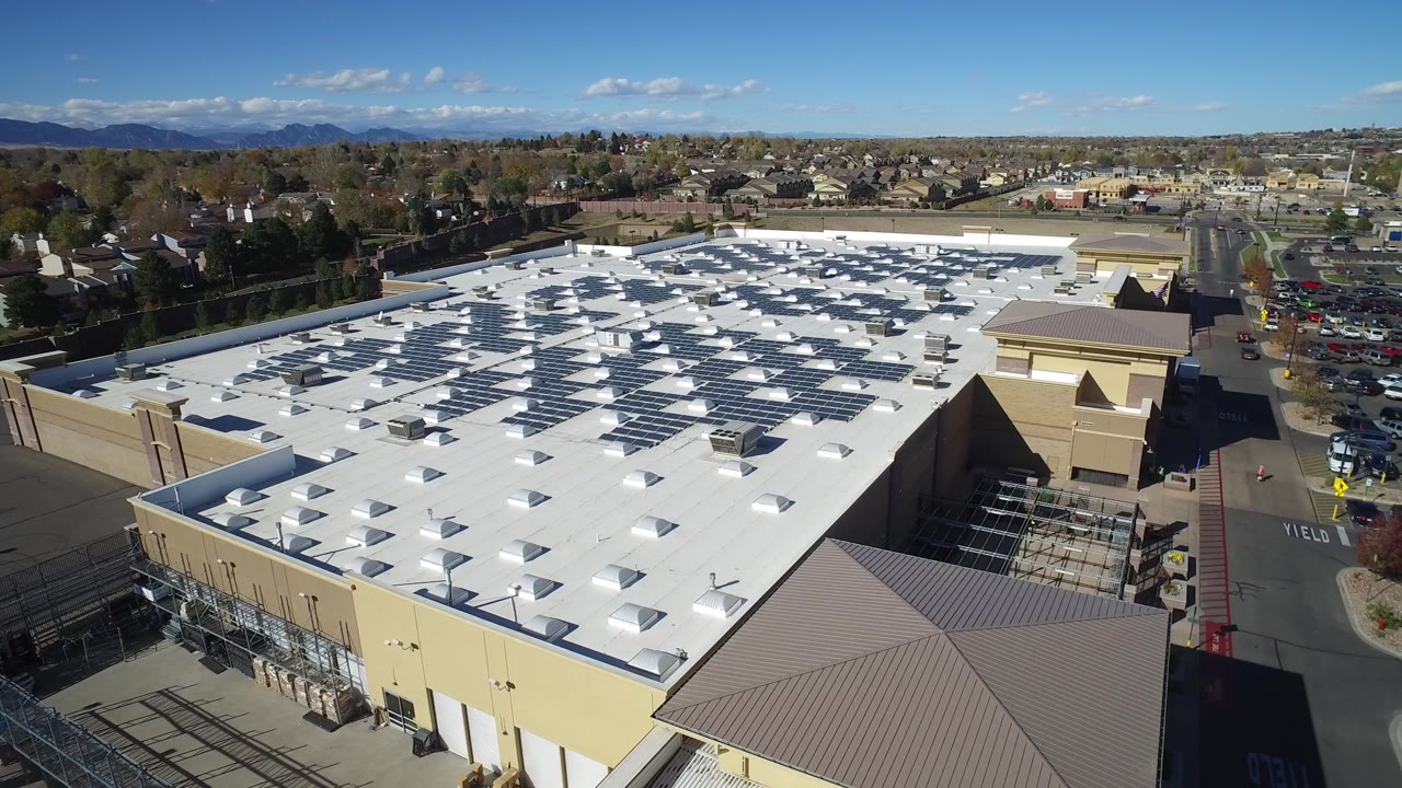 Aerial view over a large mall roof and parking area.