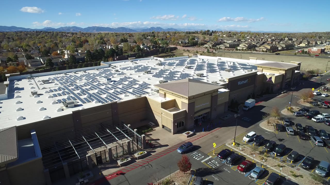 Aerial view of a Walmart shopping center parking lot with homes and mountains beyond.