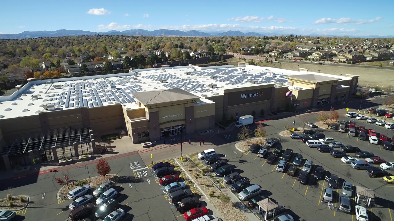 Drone-style view of a Walmart, parking lot, roads, houses, and mountains.