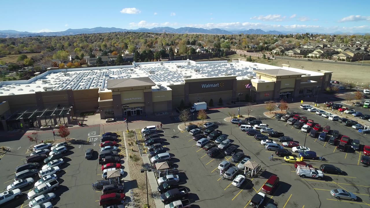 Aerial view of a Walmart store, parking lot, homes, trees, and distant mountains.