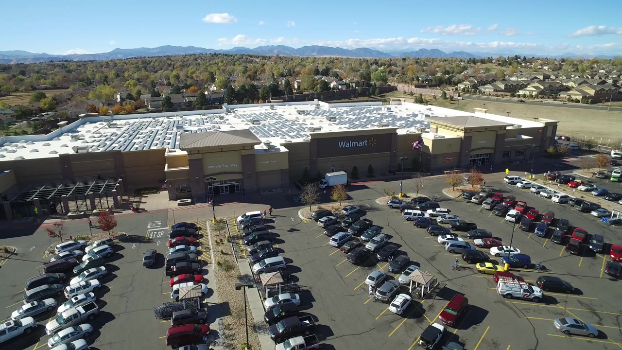 Elevated Hidden Lake, Colorado view looking across rows of parked cars toward the Walmart building, with residential streets, autumn-toned trees, mountains, and no visible people.