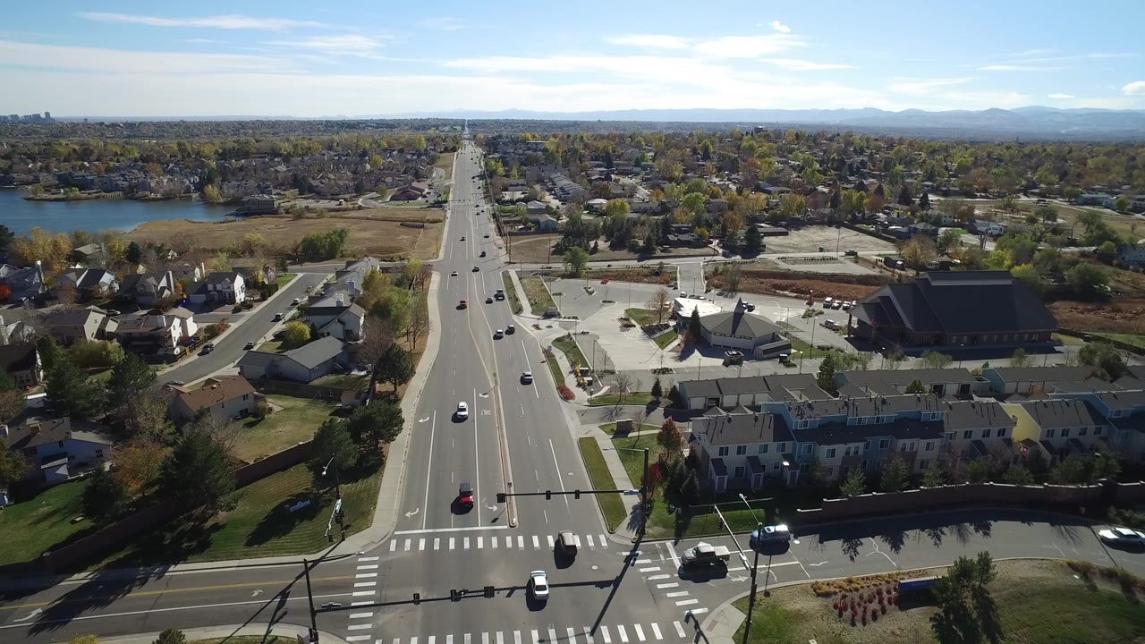Aerial view in Hidden Lake, Colorado with a broad road leading from a foreground intersection toward houses, a lake, distant skyline, and low mountains, with no visible people clearly identifiable.