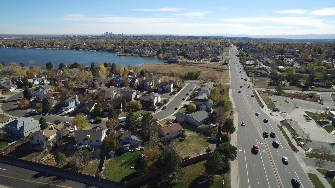 Aerial view of suburban homes beside a busy road and lake.