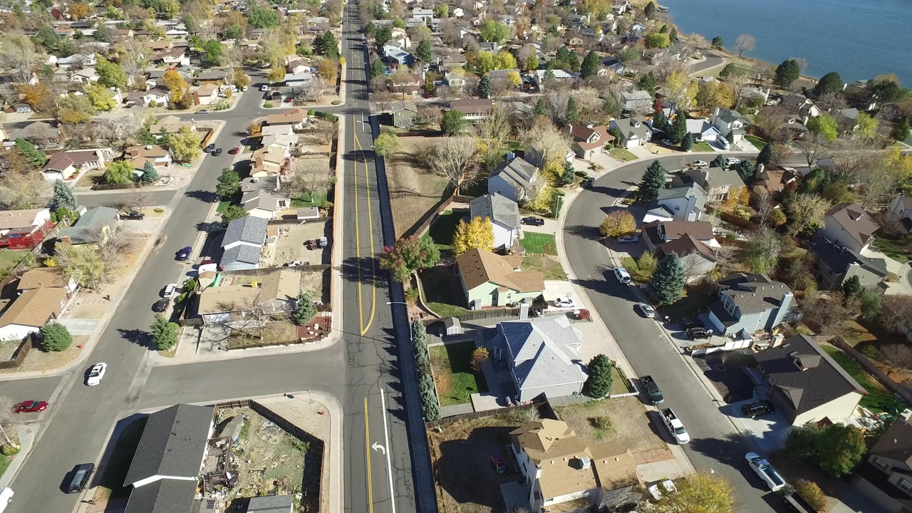 Aerial view of residential streets, houses, cars, trees, and lake water.
