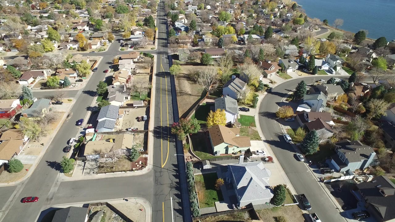 Aerial view of residential streets, houses, trees, and lake water.