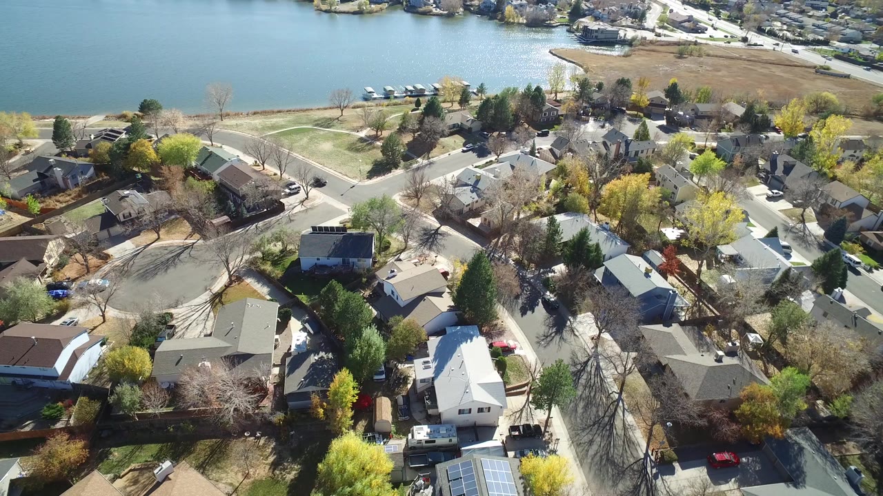 Aerial frame in Hidden Lake, Colorado, with rooftops and residential streets filling the lower frame and a broad strip of lake water and shoreline across the top.