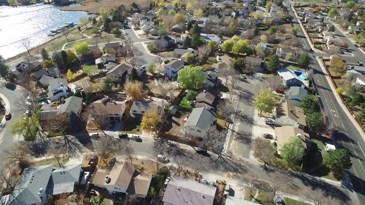 Aerial view of houses, trees, residential streets, and a lake edge.
