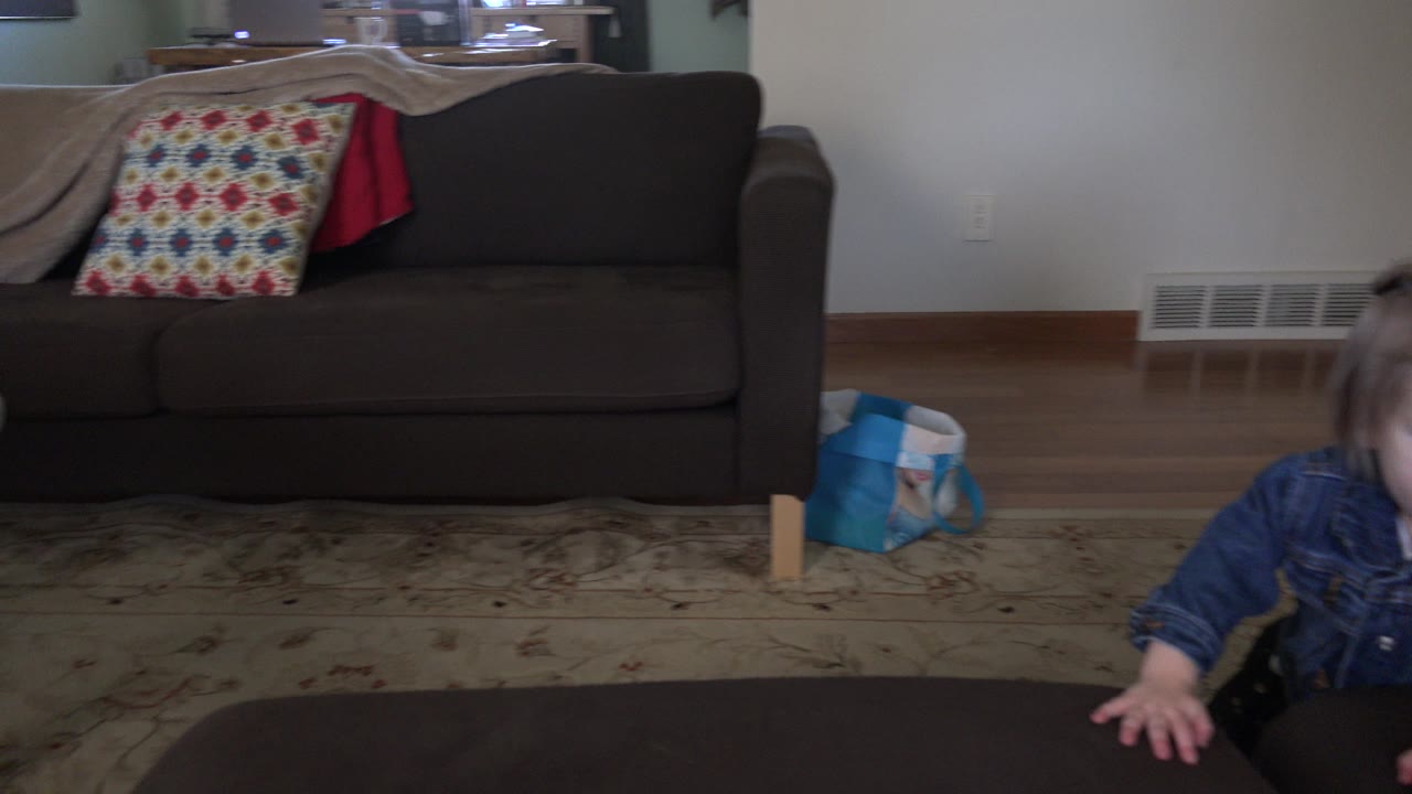 Toddler partly visible behind a dark ottoman in a living room.
