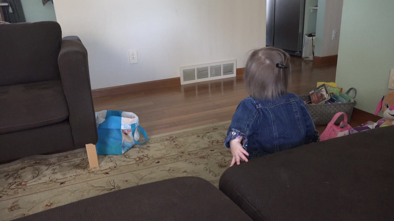 Young child seen from behind in a living room near brown furniture.