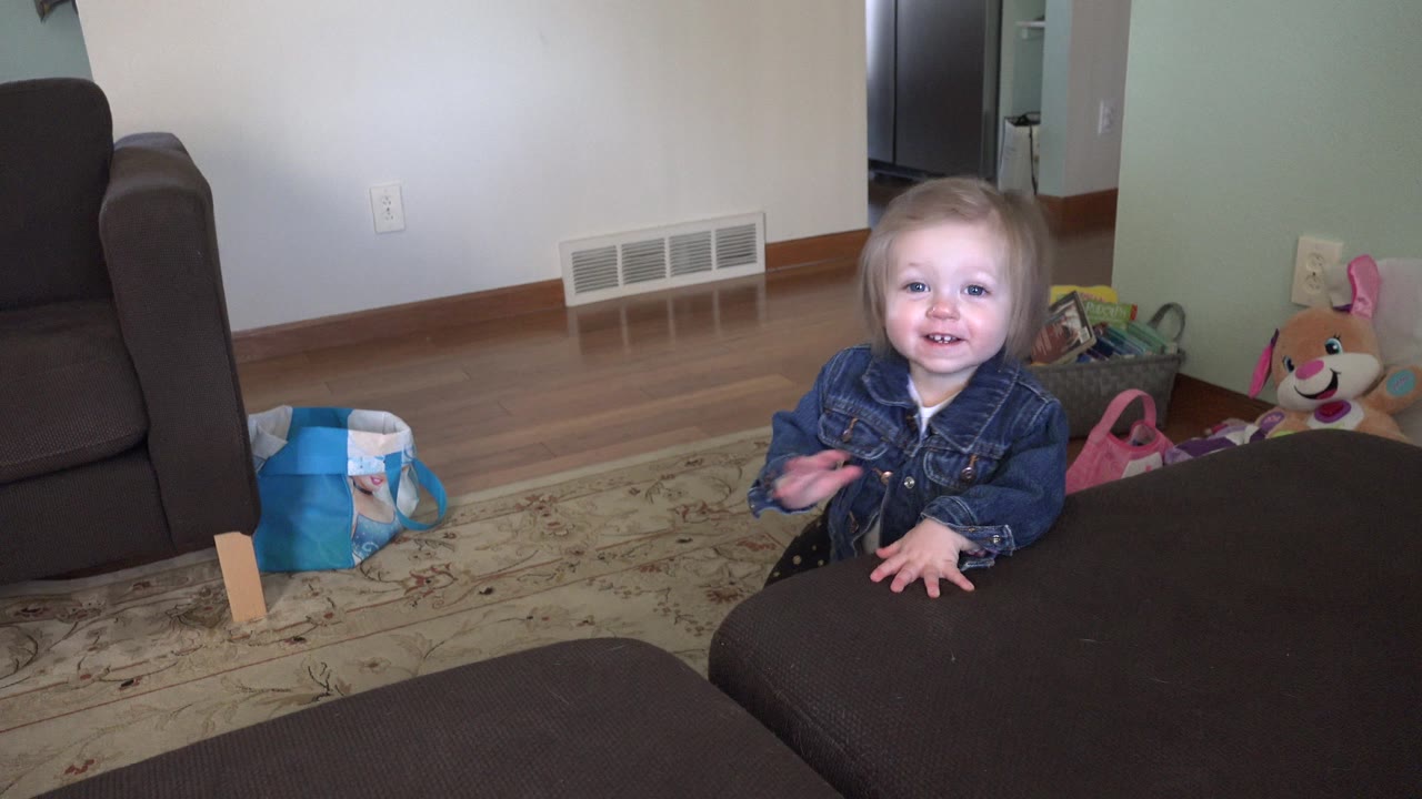 Young child smiling on a living room carpet near dark furniture and toys.