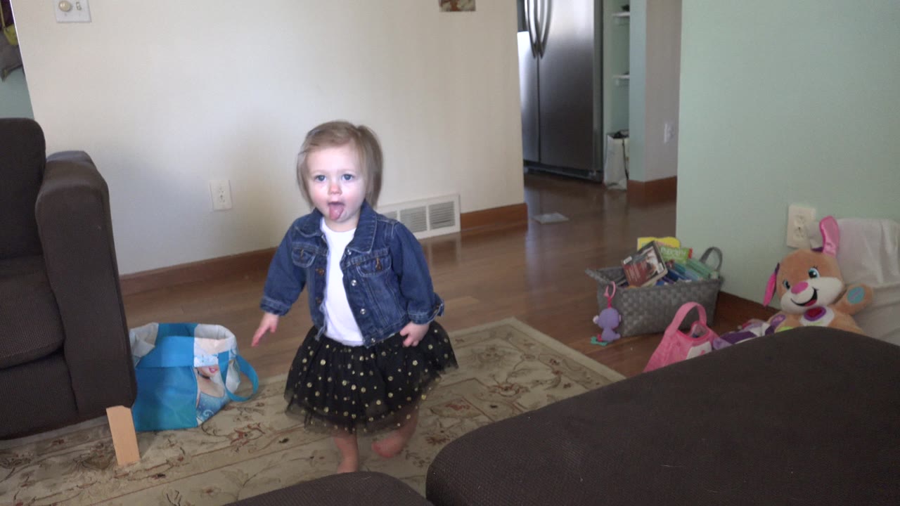 Toddler girl standing in a living room near a grey couch.