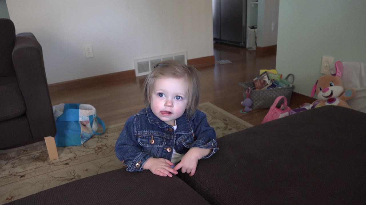 Young child standing by dark furniture in a toy-filled room.
