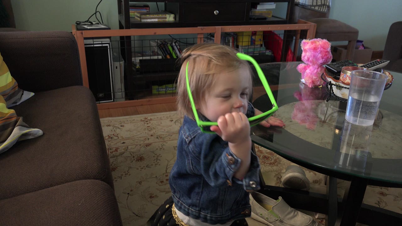 Young girl holding bright green sunglasses near a glass table.