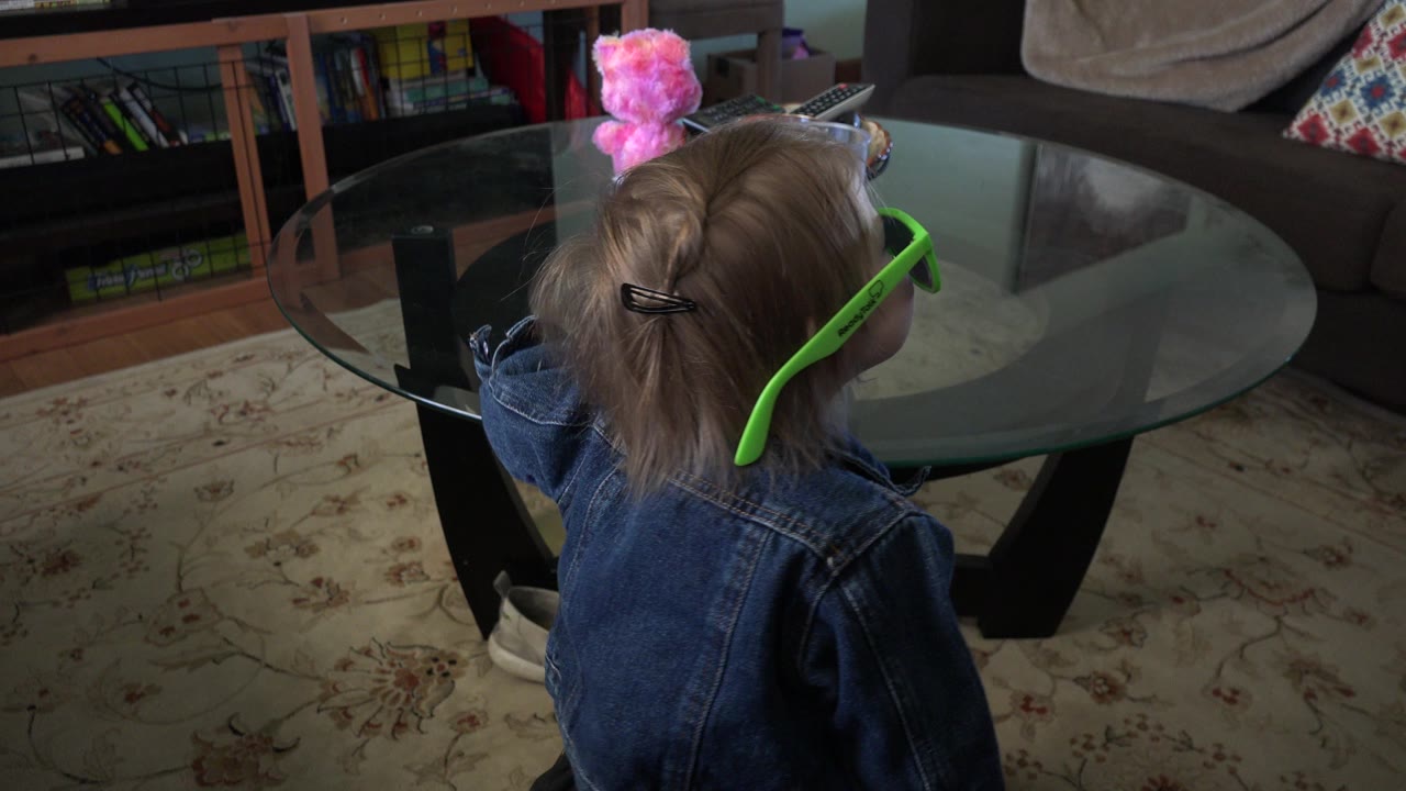 Toddler in green sunglasses near a glass coffee table.