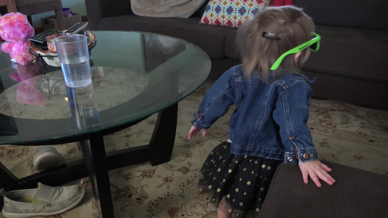 Toddler in green glasses near a glass coffee table in a living room.