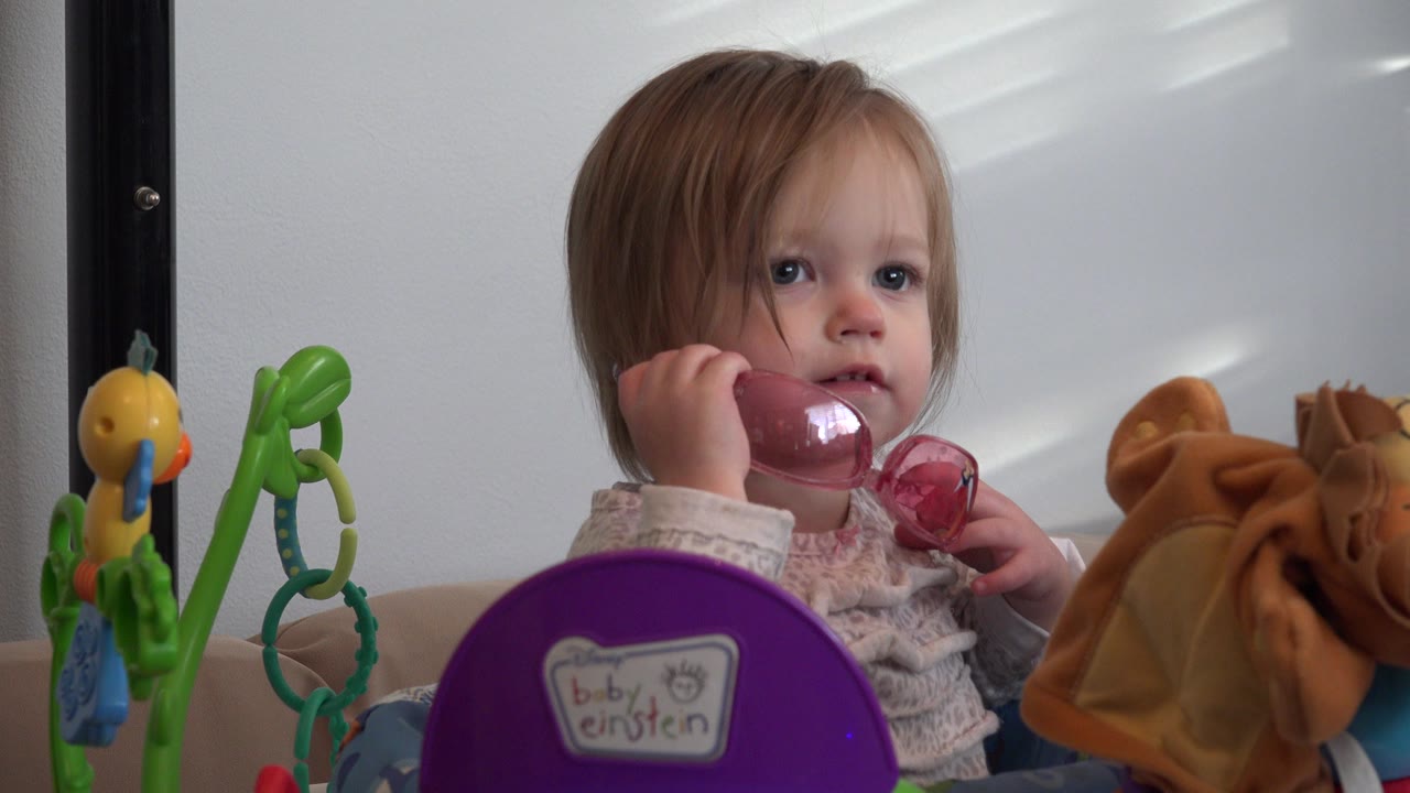 Toddler holding pink glasses among toys indoors.