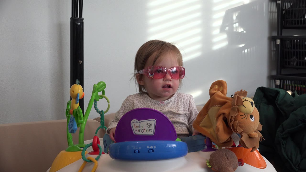 Toddler in pink sunglasses behind activity toys indoors.
