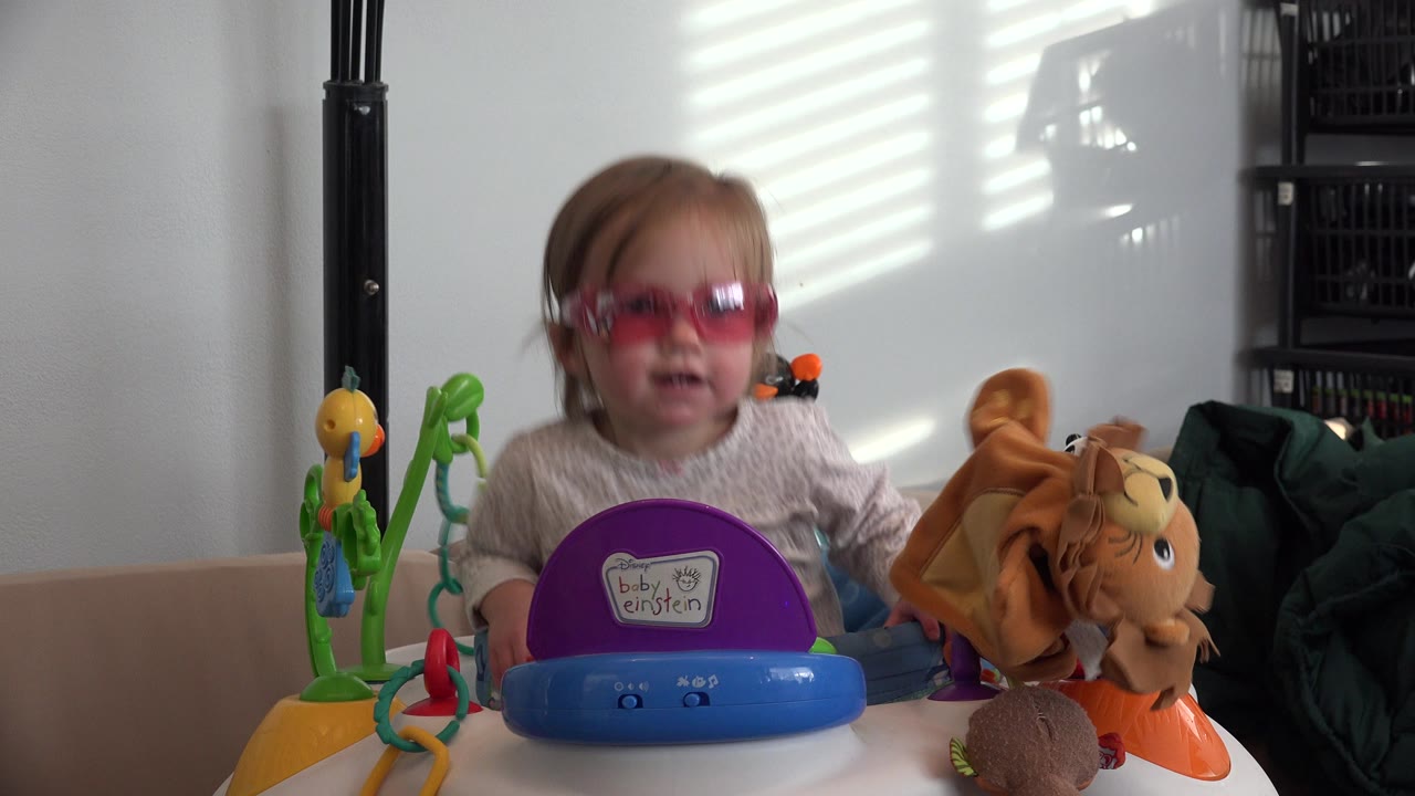 Toddler in pink sunglasses behind colorful toys indoors.