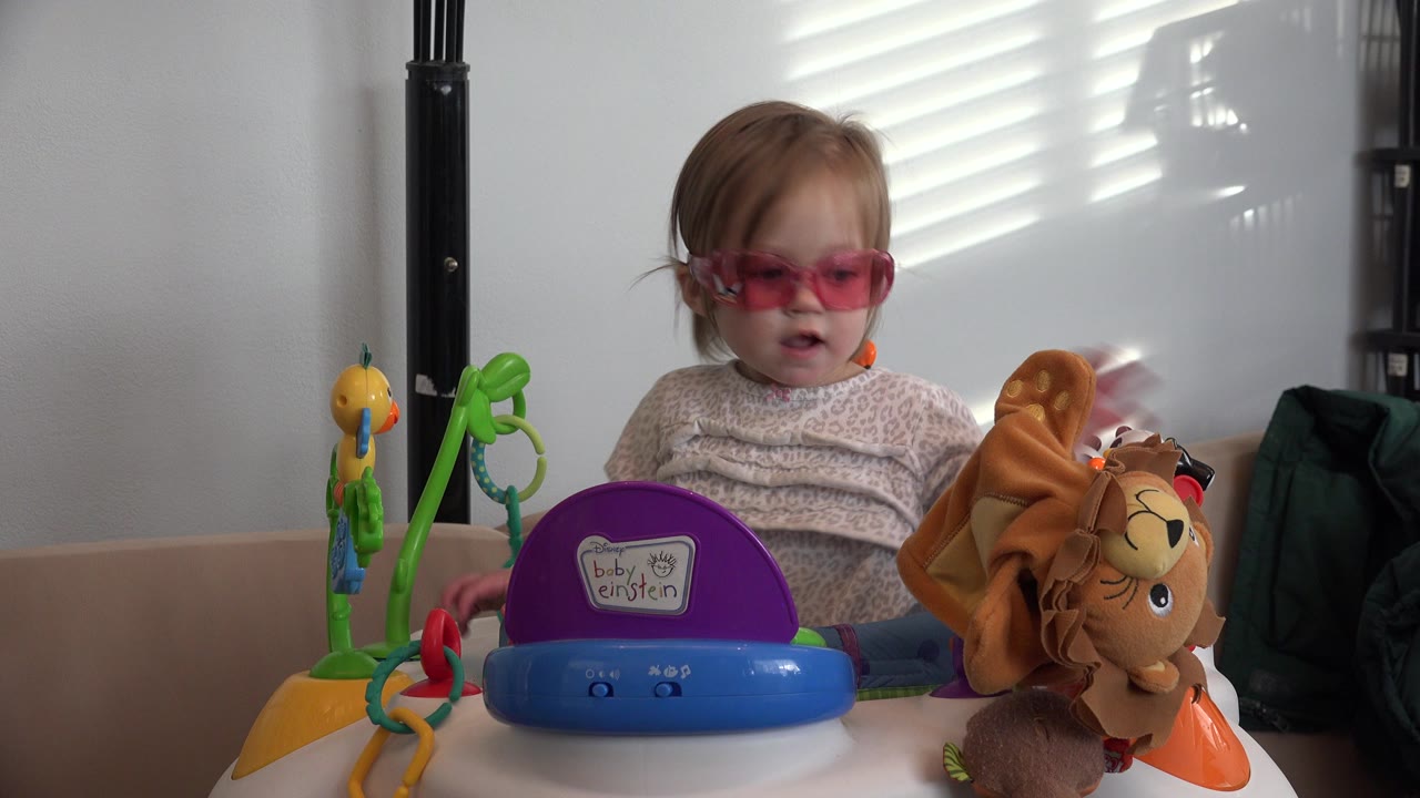 Young child in pink glasses seated behind colorful toys.